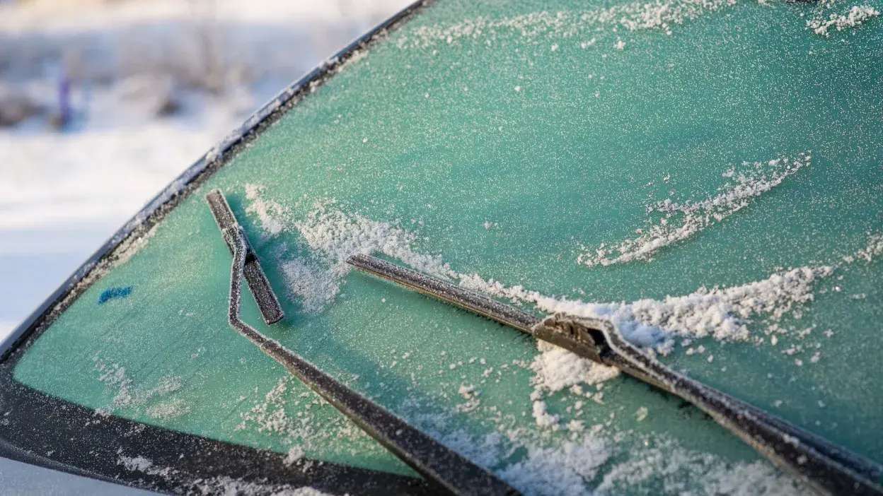 Parabrisas de carro com gelo e neve, com limpa-vidros a remover a camada congelada.