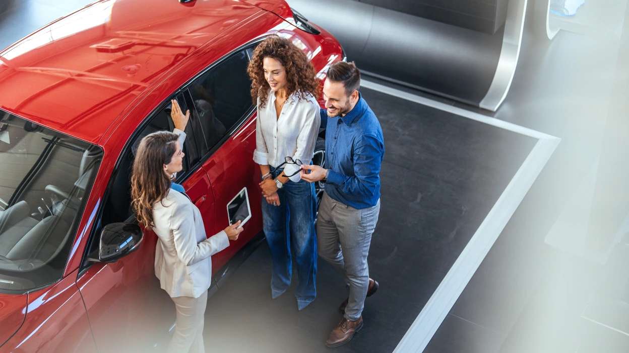 vendedora de carros num stand a mostrar carro vermelho a um casal