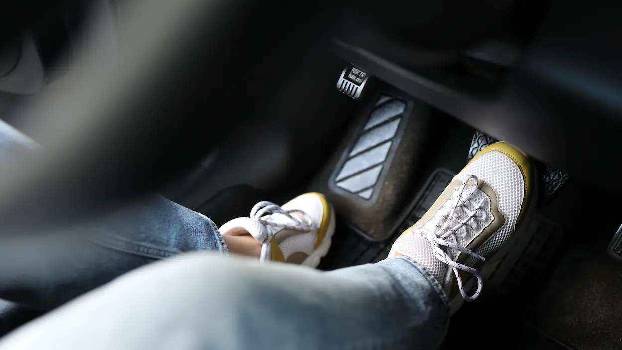 foco nos ténis de um condutor enquanto ele pressiona o pedal do travão do carro