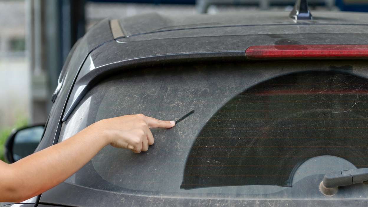 pessoa a passar o dedo na sujidade do vidro traseiro de um carro que está cheio de pó